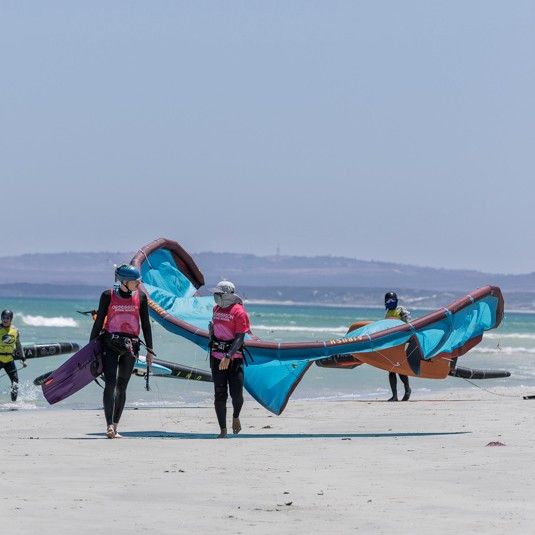 Two instructors carrying a kite along the beach before a lesson