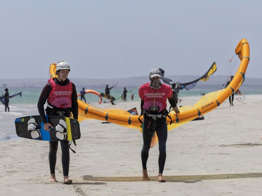 Two instructors carrying a wing and foil boards down the beach