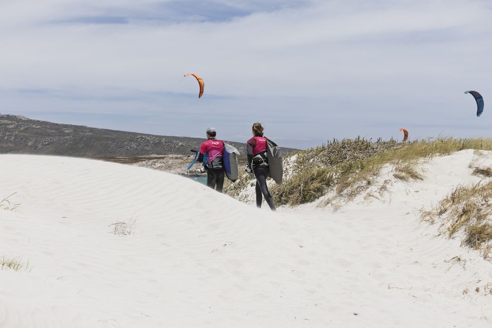 A rider carrying a kite over the white dunes above the lagoon