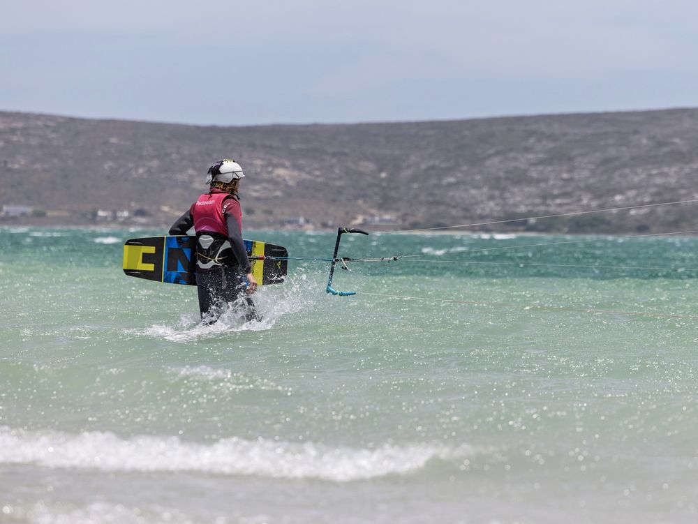 A rider walking out into the lagoon carrying a foil board