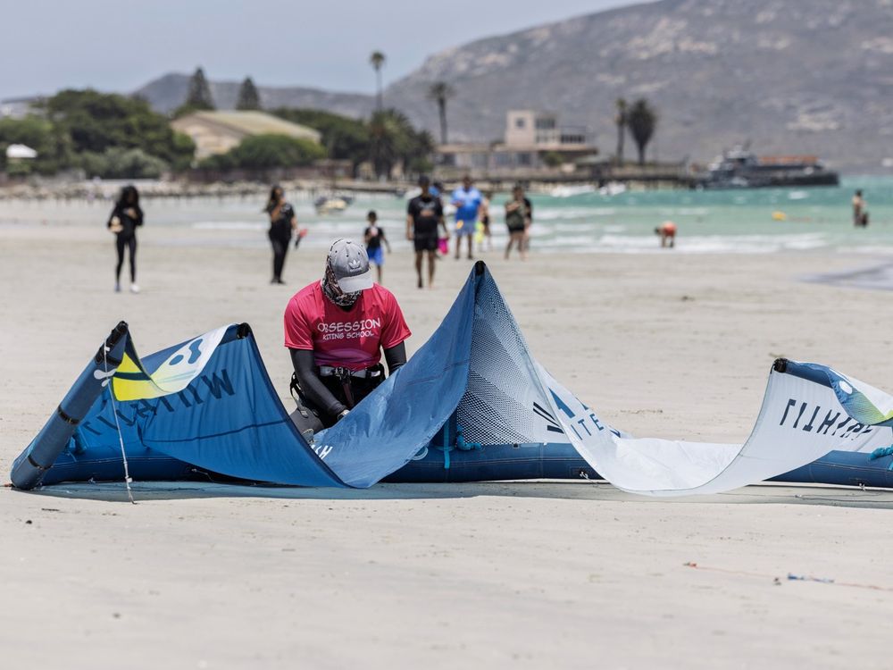 An instructor laying a kite out on the sand with the beach busy behind
