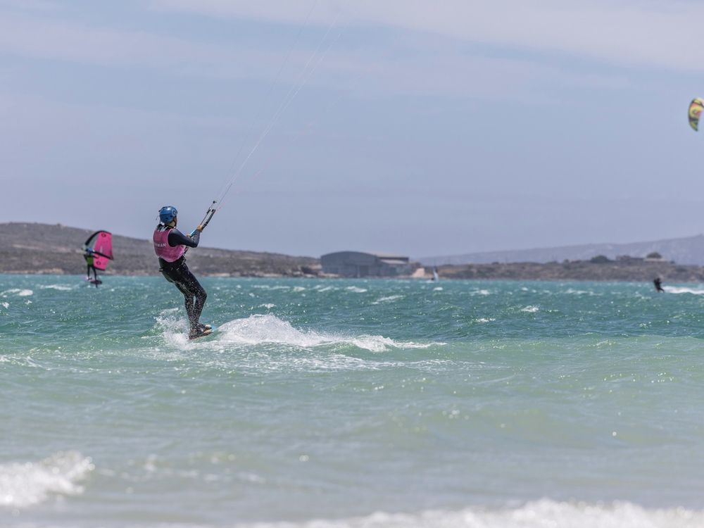 A kitesurfer riding across the lagoon with the hills behind