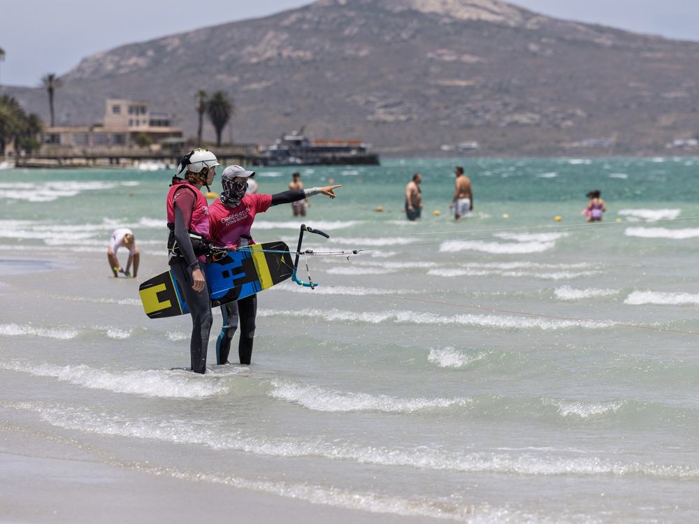 An instructor and student walking back up the beach with board and kite