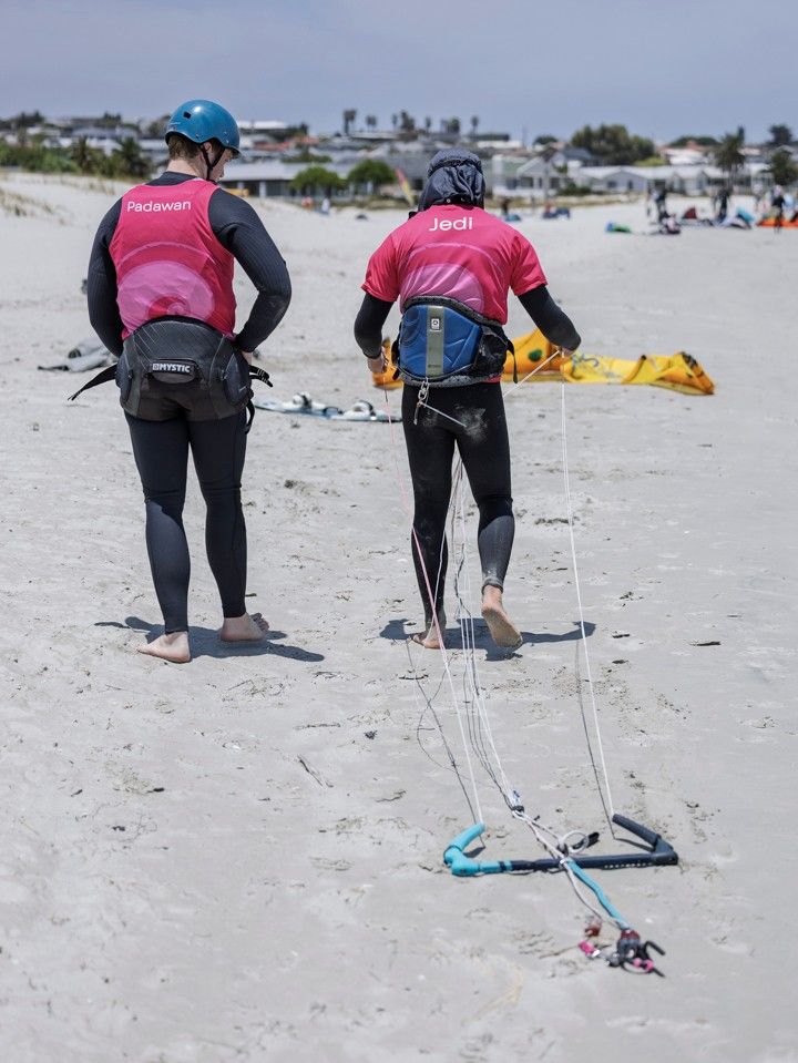 Two riders walking up the beach towards a kite laid out on the sand