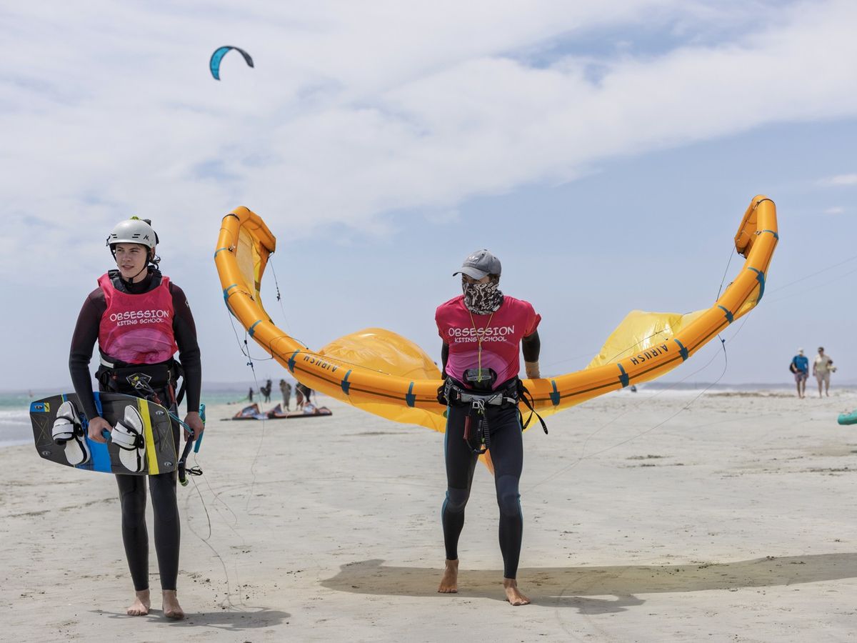 Two Obsession Kiting instructors carrying a wing along the beach at Langebaan