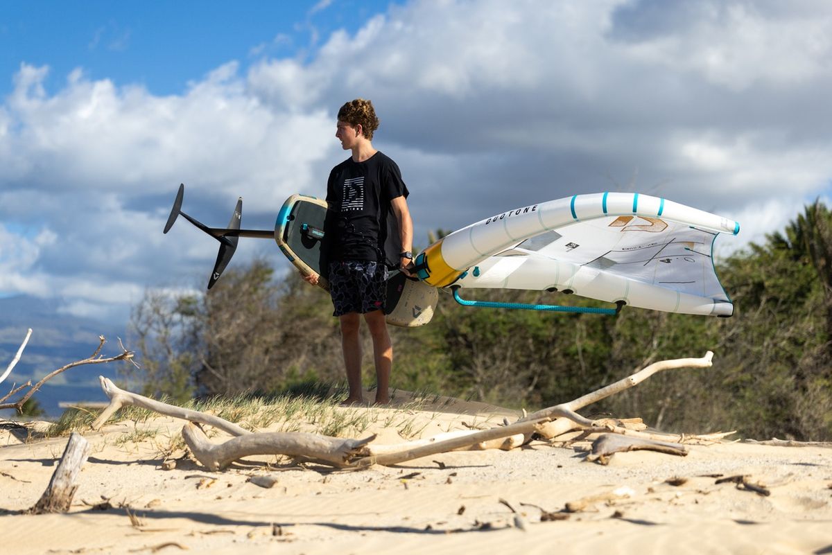 A rider carrying a complete Duotone wing setup — wing, foil board and foil