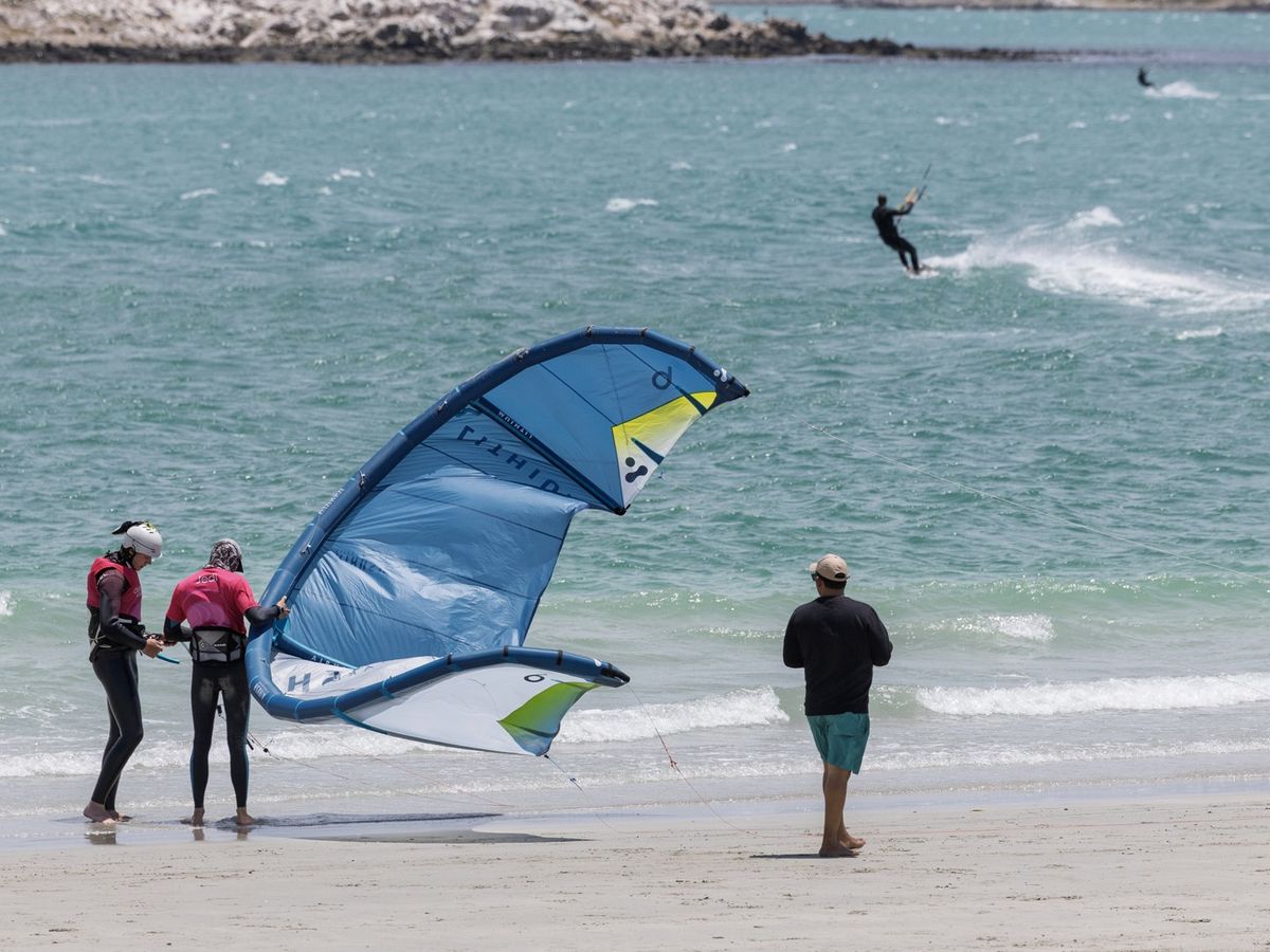 A wing held on the beach at Langebaan, with a kitesurfer riding on the lagoon behind